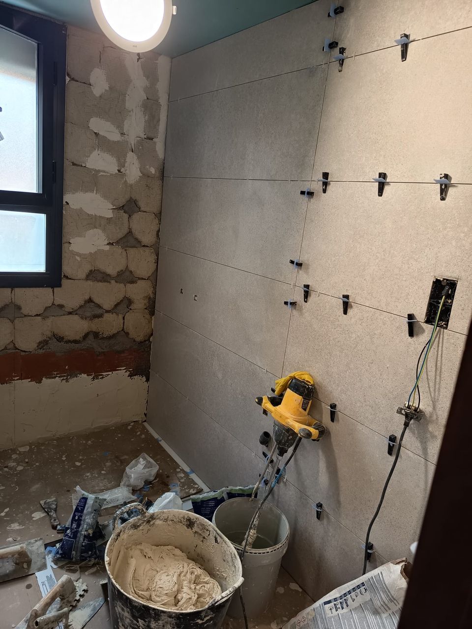 El baño al inicio de la obra: paredes picadas hasta el ladrillo, primeras piezas de porcelánico colocadas y herramientas en el suelo