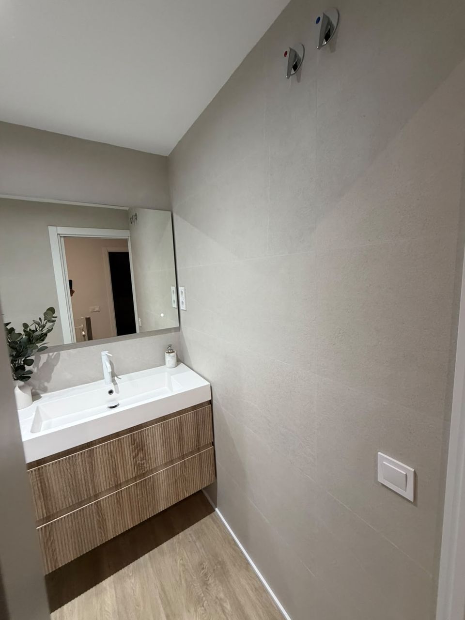 Mueble de lavabo de madera estriada con lavabo encastrado blanco y pared en porcelánico gris claro