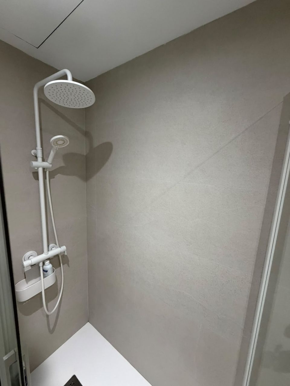 Detalle de la columna de ducha blanca con rociador redondo sobre porcelánico gris claro