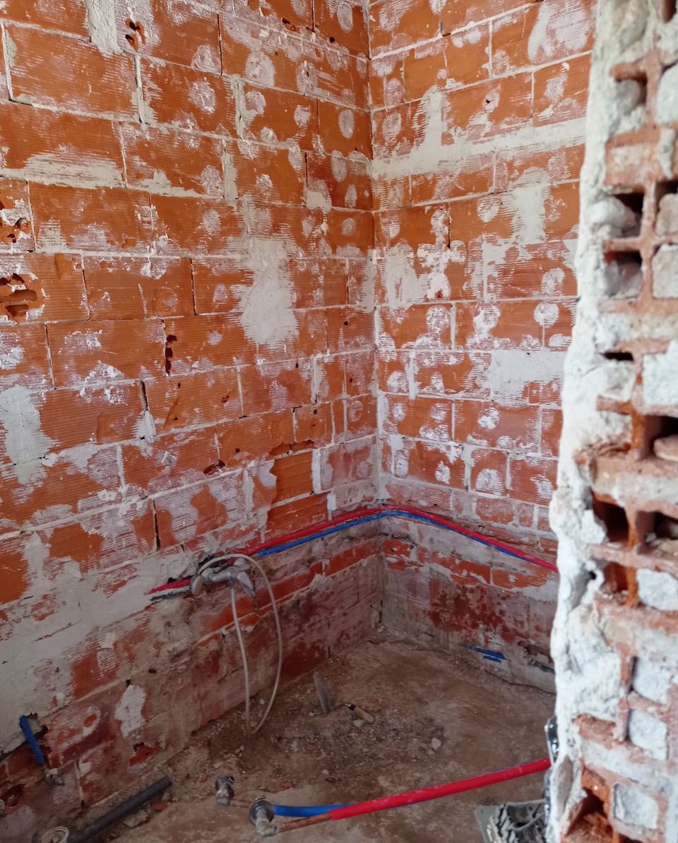 El mismo baño antes de la reforma, con las paredes en ladrillo visto y las tuberías a la vista