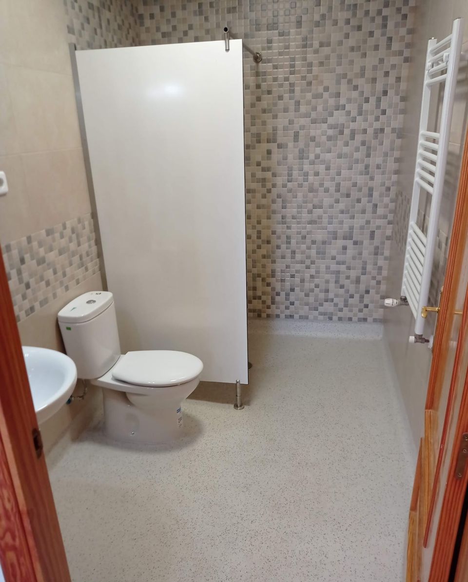 Baño adaptado terminado: ducha abierta con mampara fija, mosaico gris, suelo continuo antideslizante, inodoro, lavabo y radiador toallero