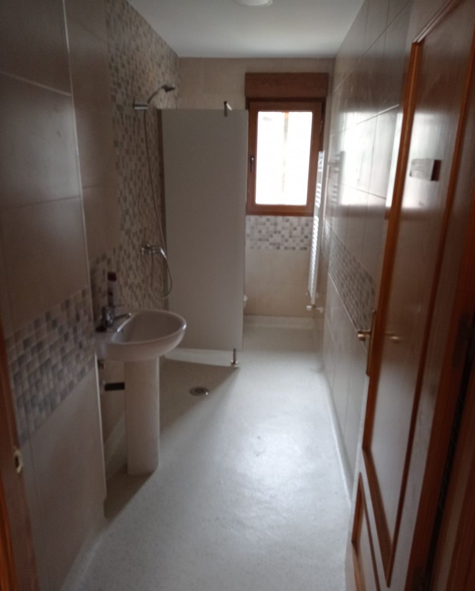 Baño adaptado terminado: ducha a ras de suelo con mampara, lavabo de pedestal, radiador toallero y cenefa de mosaico