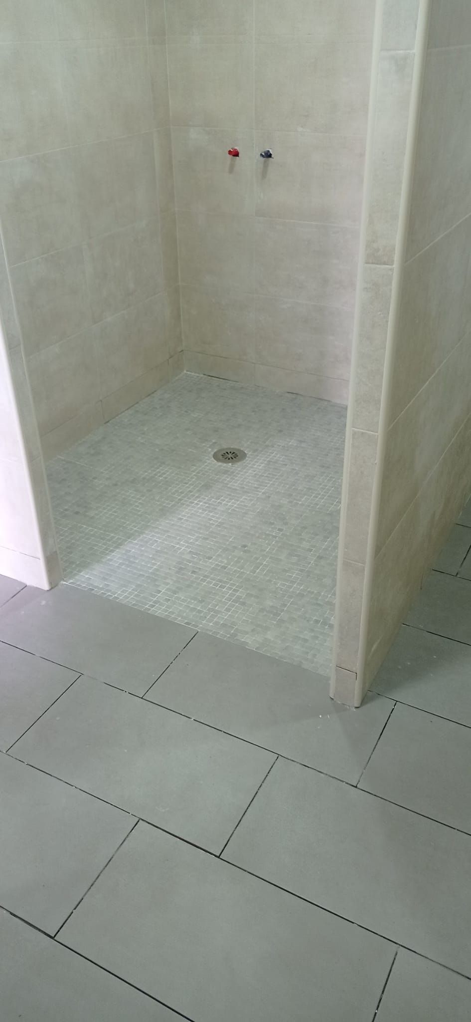 Ducha de obra terminada: plato enrasado con el suelo, mosaico antideslizante y paredes en porcelánico claro