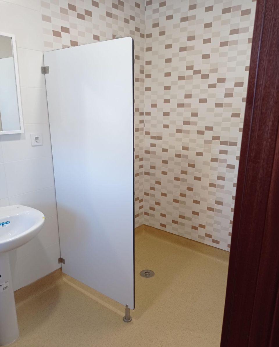 Baño adaptado terminado: ducha a ras de suelo con mampara fija, suelo antideslizante y mosaico en tonos beige