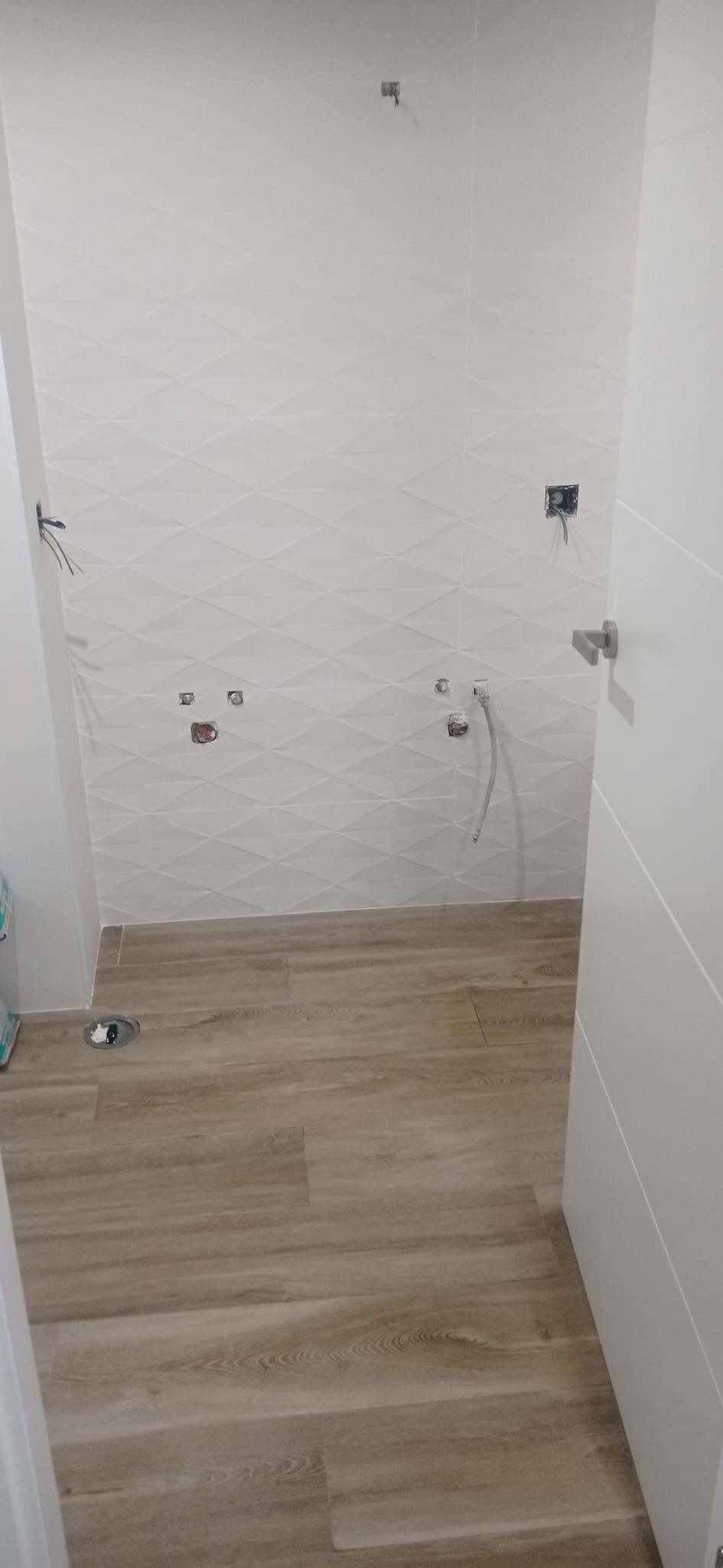 El baño durante la obra: azulejo blanco con relieve geométrico y suelo porcelánico efecto madera recién colocados, con las tomas de agua preparadas
