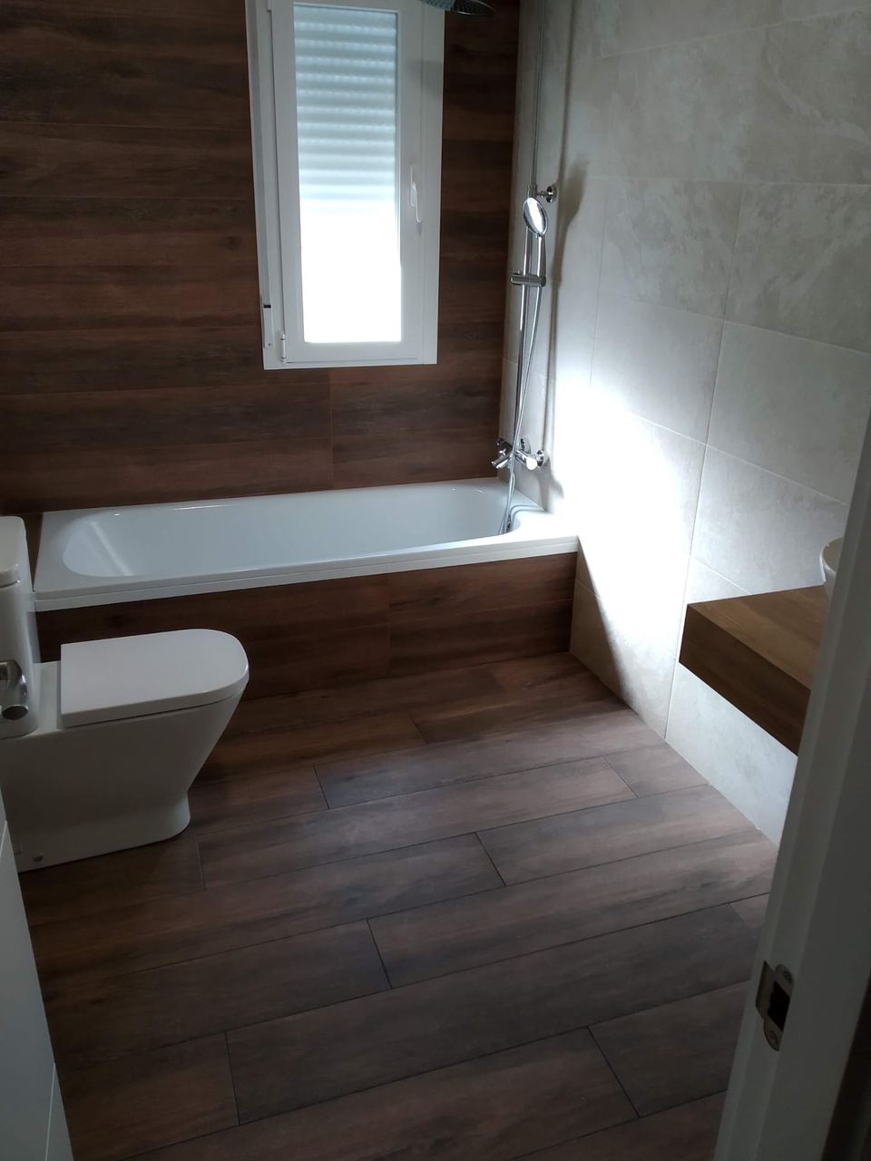 Baño con bañera, suelo efecto madera y ventana