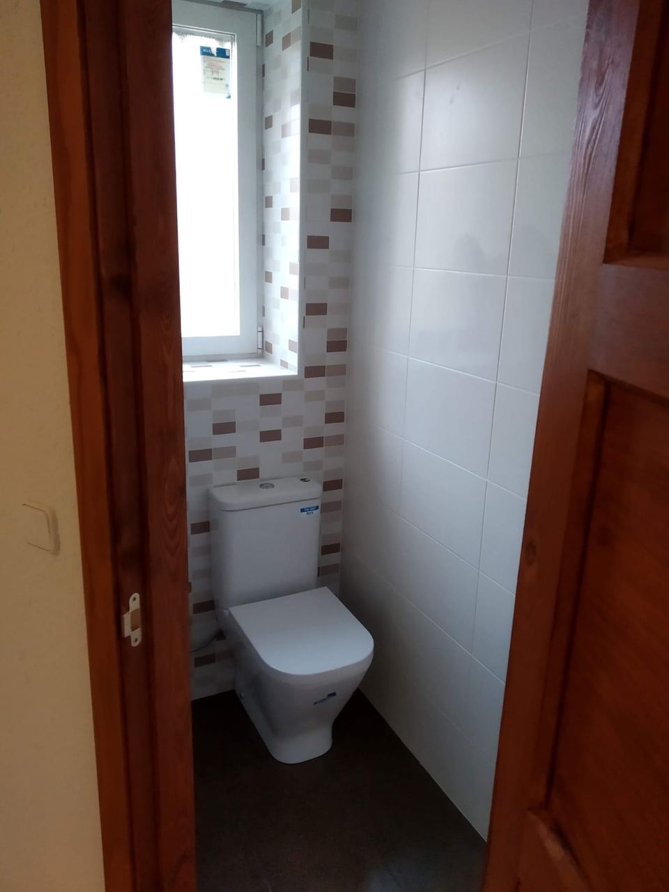 El mismo baño reformado: azulejo blanco de gran formato e inodoro nuevo