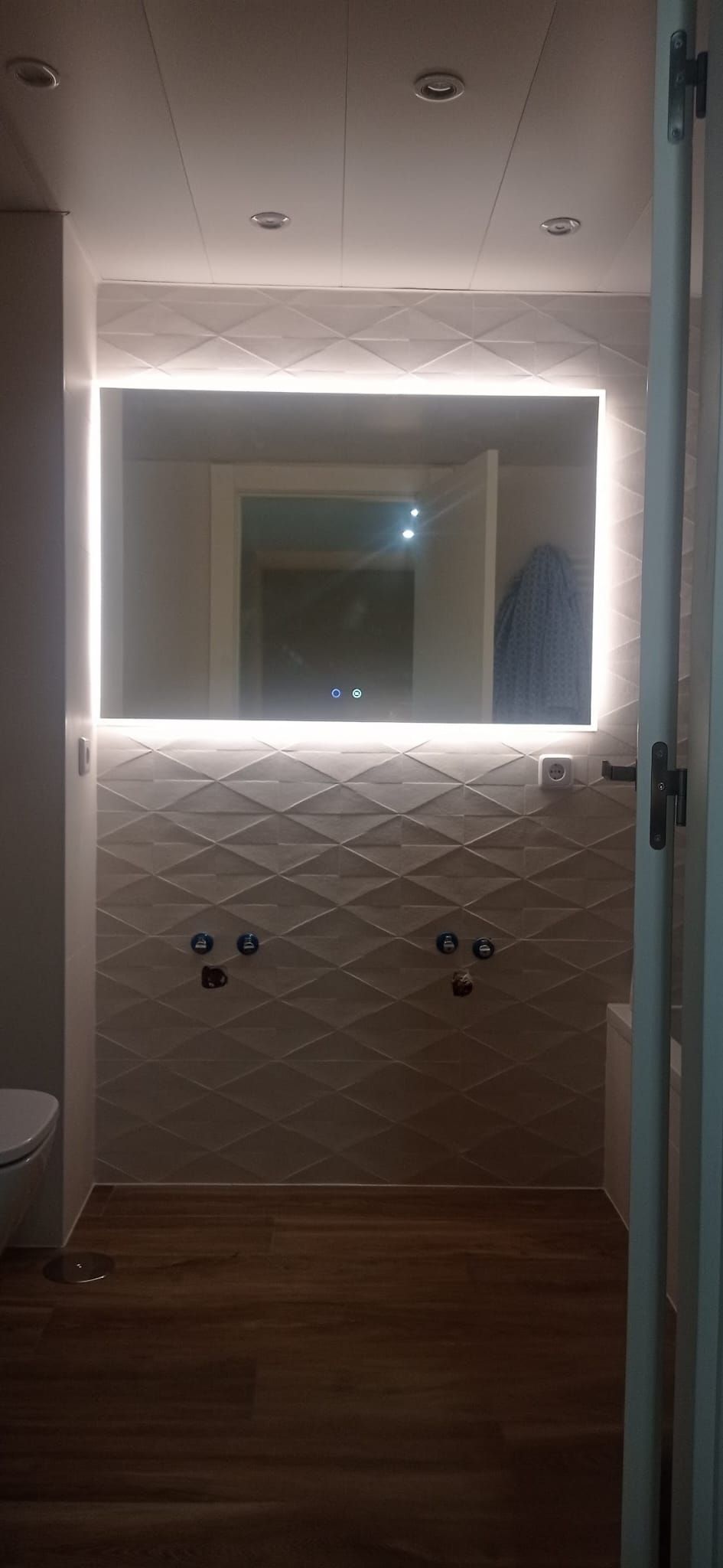 El mismo baño con el espejo retroiluminado y los focos del techo instalados sobre el azulejo en relieve
