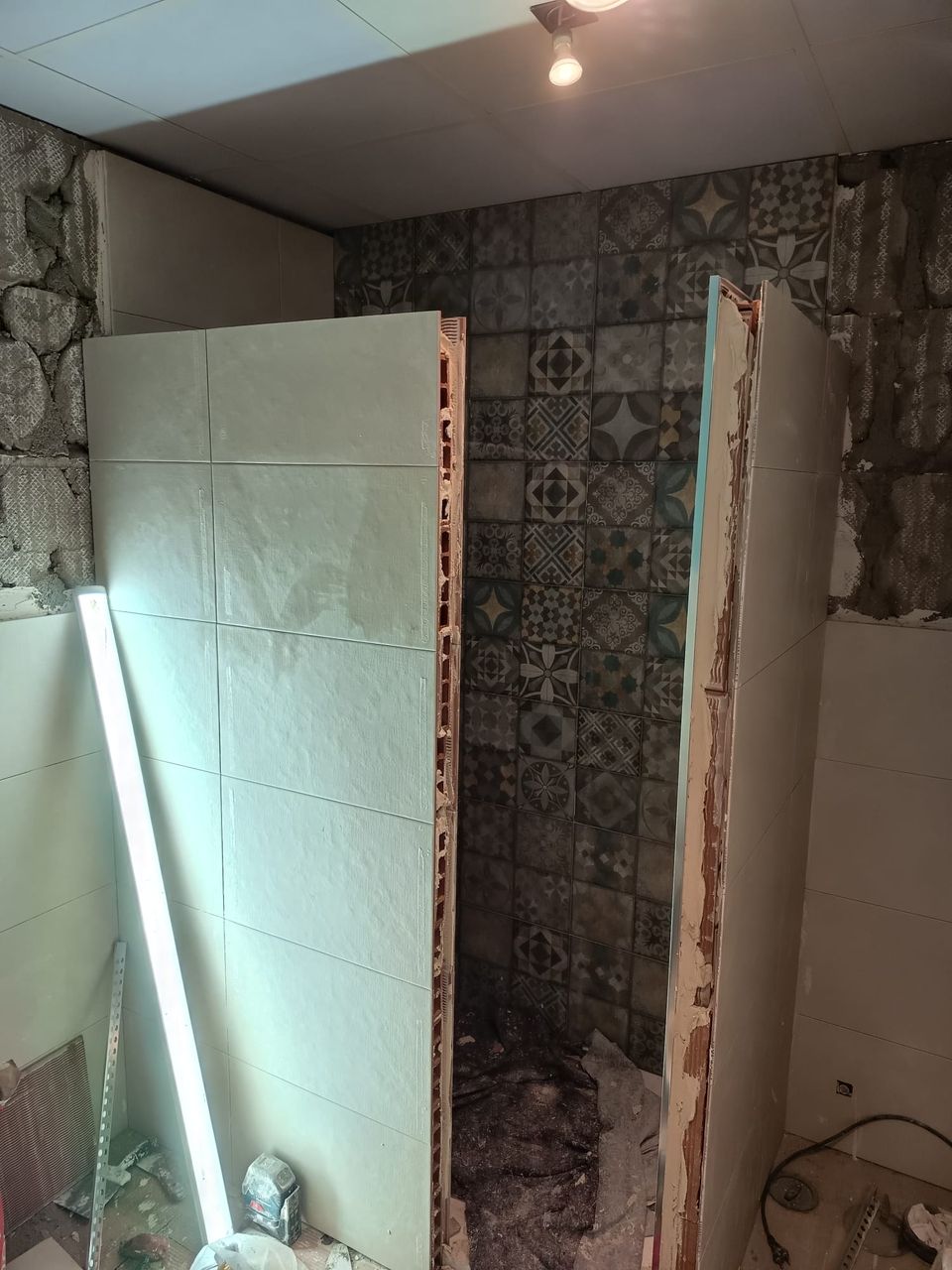 La ducha durante la obra: azulejo hidráulico ya colocado al fondo y porcelánico claro en los tabiques laterales, con las paredes del baño aún picadas