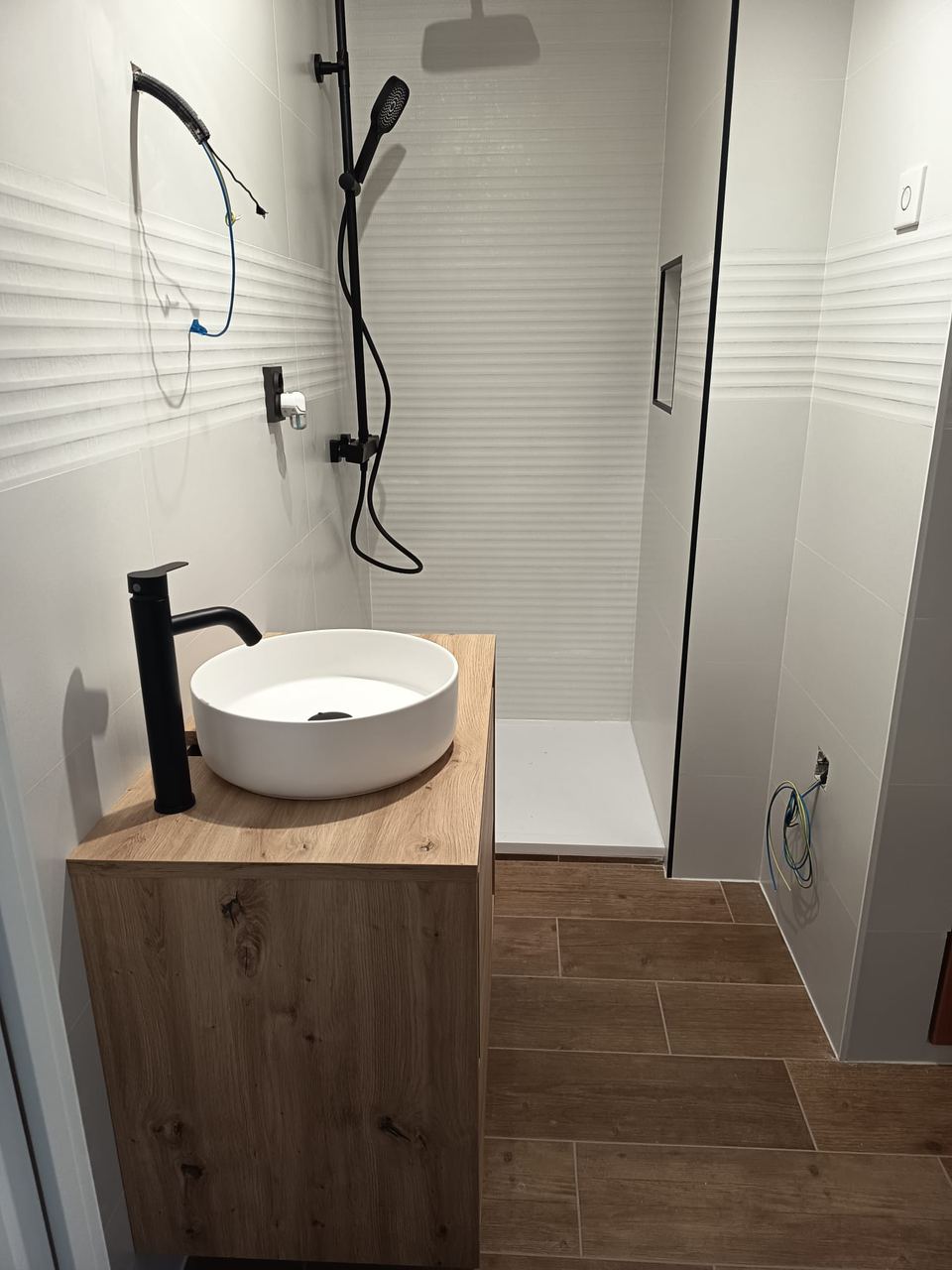 Baño con lavabo sobre encimera de madera, grifería negra y ducha de obra