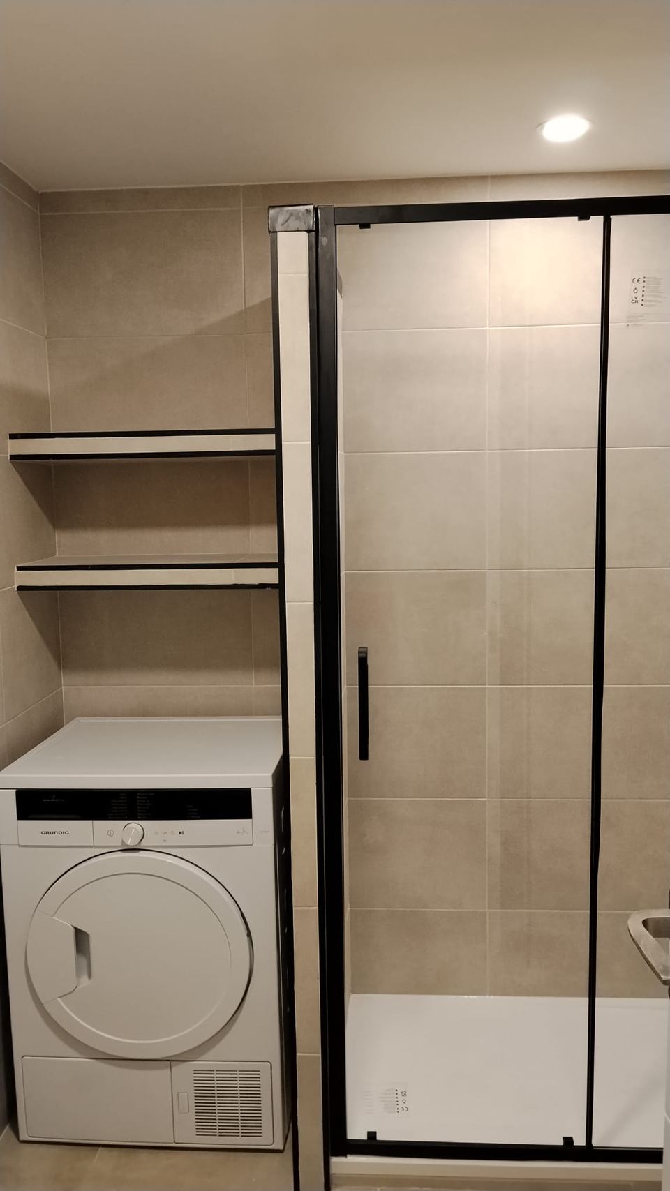 Baño terminado con la lavadora integrada bajo baldas a medida y azulejo porcelánico arena
