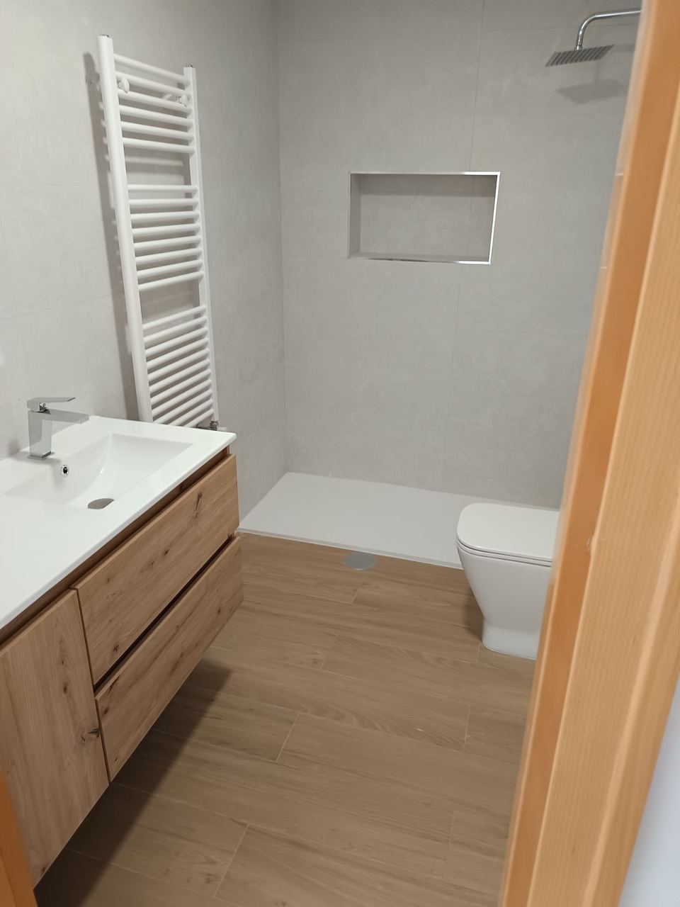 Baño terminado con mueble de madera, radiador toallero y hornacina en la ducha