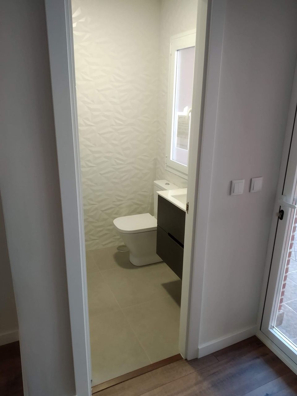 Baño terminado con azulejo blanco en relieve y mueble suspendido