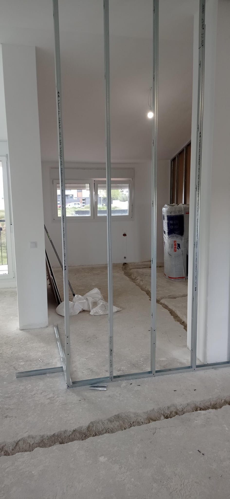 Estructura metálica de los tabiques de pladur en la buhardilla diáfana, con la ventana al fondo y el aislamiento preparado