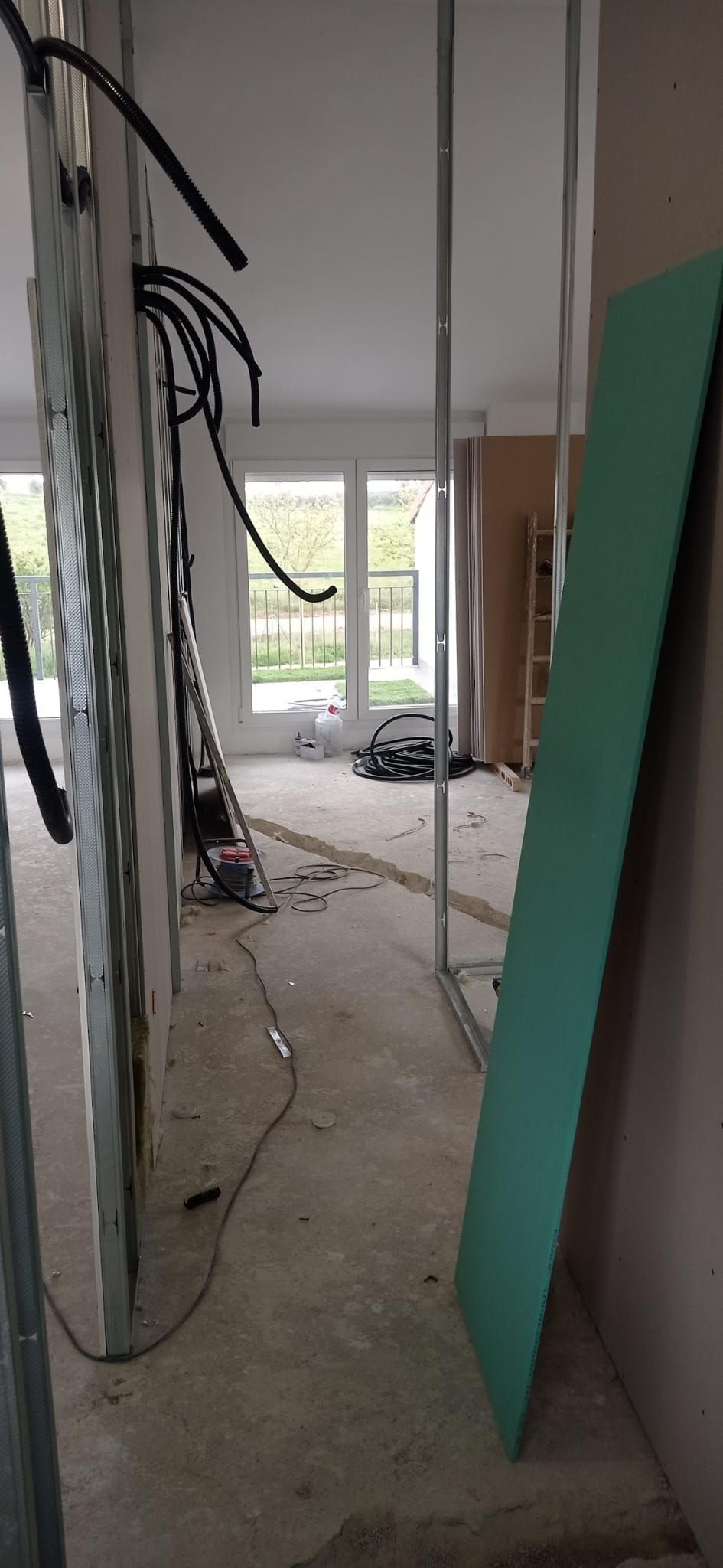 Paso entre dos estancias nuevas durante la obra, con el cableado eléctrico preparado y la salida a la terraza al fondo