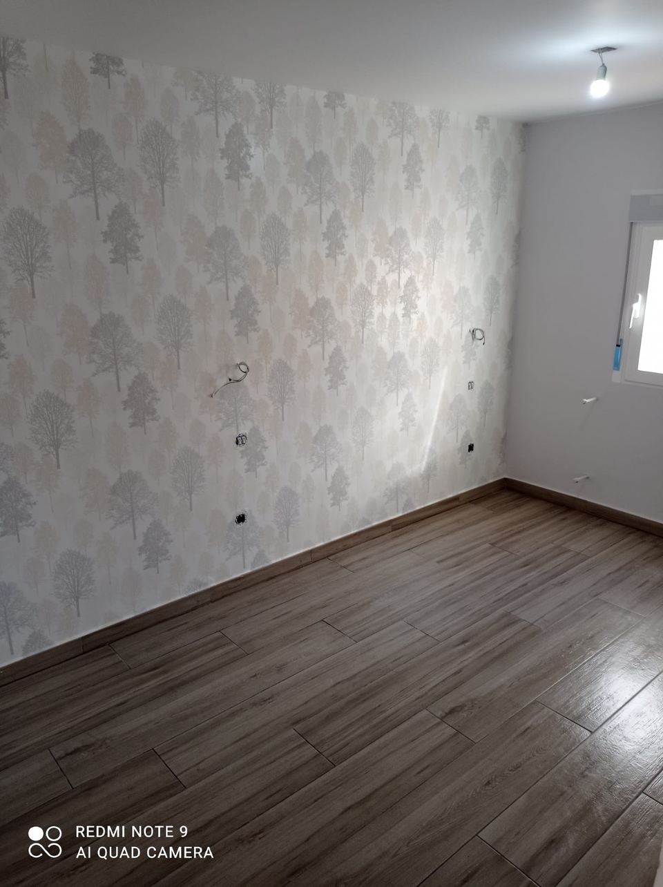 Dormitorio con papel pintado gris y suelo efecto madera