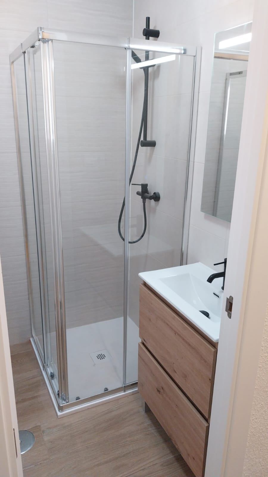 Ducha de obra nueva con mampara y mueble de lavabo en madera