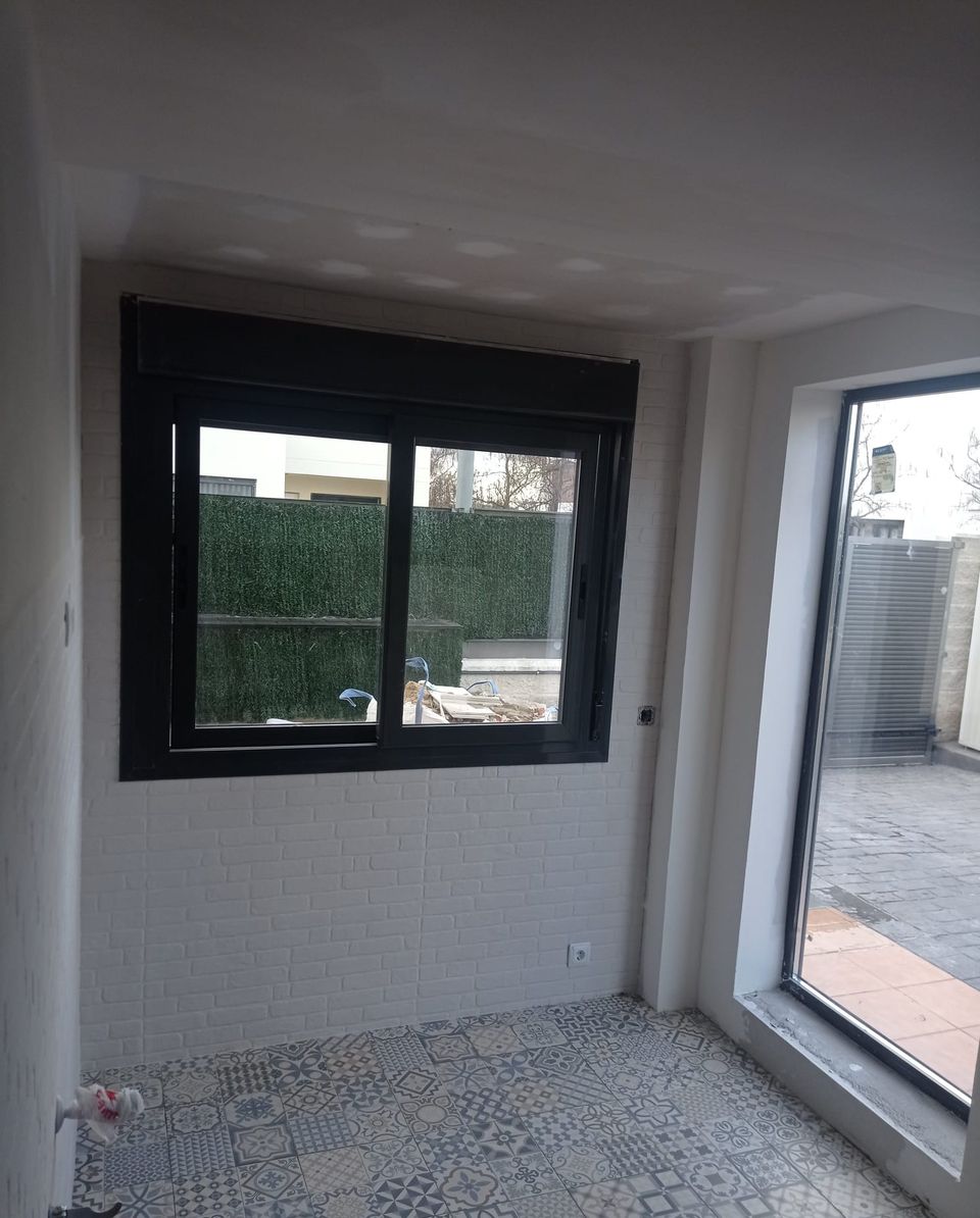 Estancia ganada al porche, casi terminada: ventana corredera negra, revestimiento de ladrillo blanco, suelo hidráulico y puerta acristalada al patio