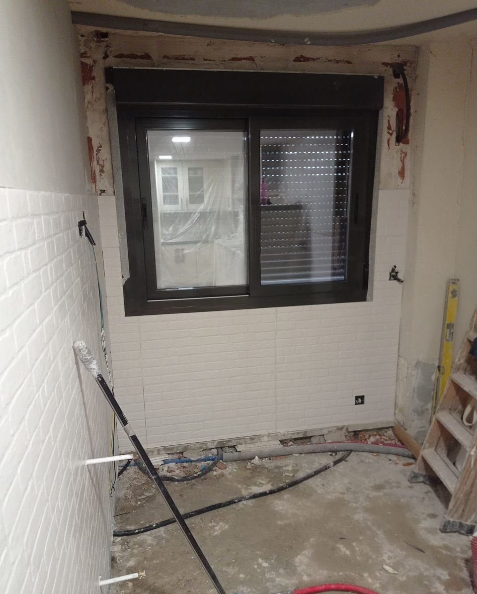 La misma estancia durante la obra: ventana nueva colocada y revestimiento de ladrillo blanco a medio poner, con el suelo aún sin solar