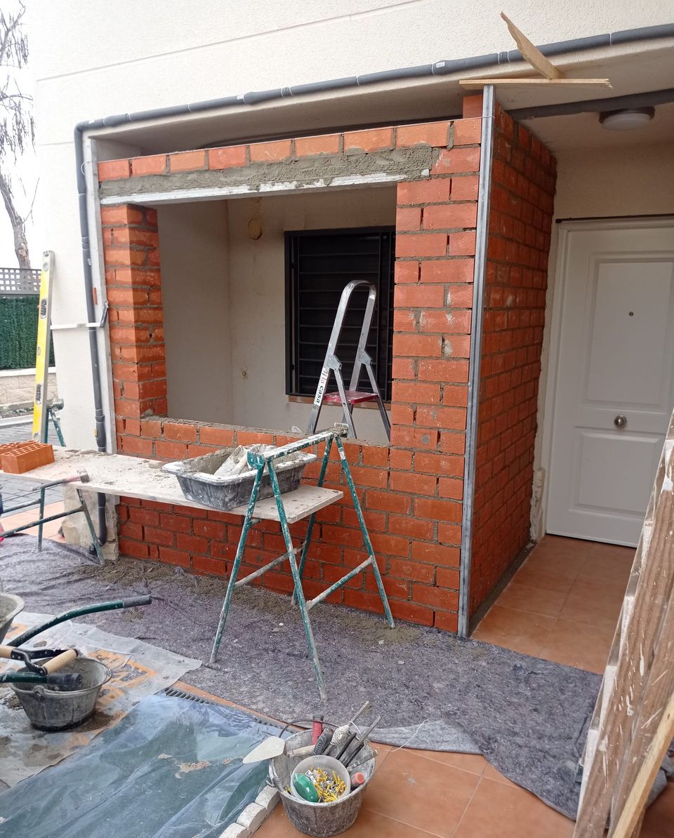 Exterior de la vivienda durante el cerramiento del porche con ladrillo, junto a la puerta de entrada