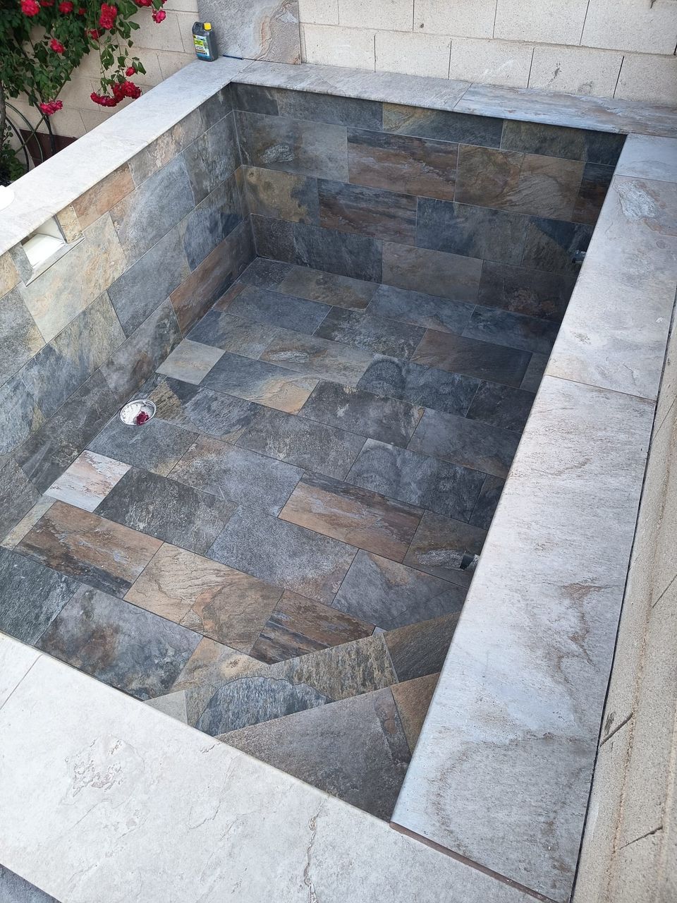 Piscina de obra terminada vista desde la esquina, con revestimiento porcelánico efecto piedra y coronación en piedra clara