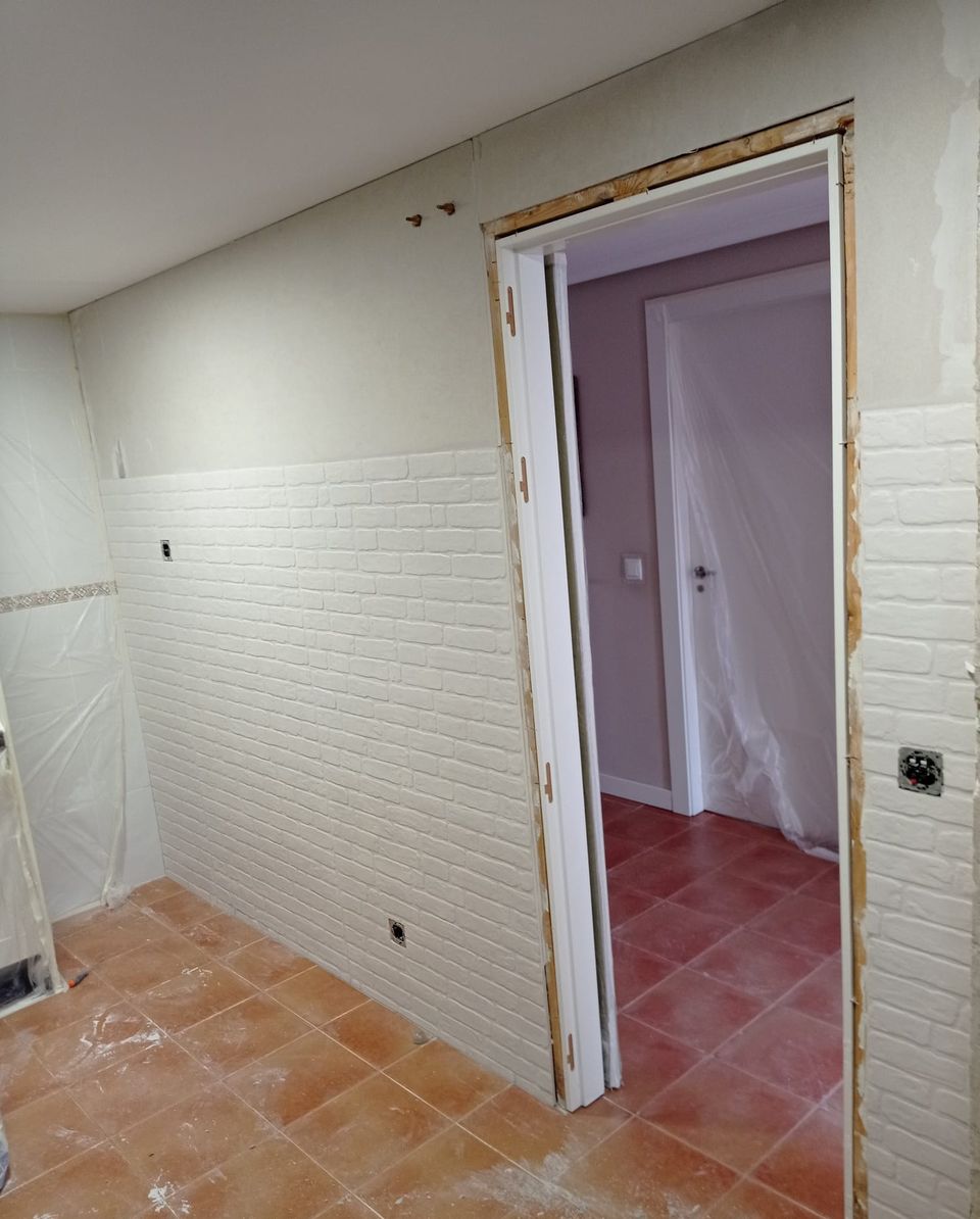 Tabique con revestimiento de ladrillo blanco y marco de la puerta recién colocado, sobre el suelo antiguo de barro