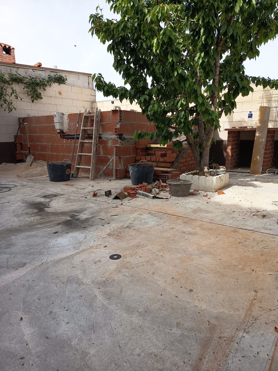 Muros de ladrillo de la piscina en construcción, con escalera de mano y cubos de mortero en el patio