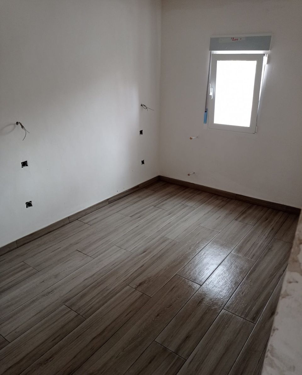Dormitorio en reforma con paredes lisas recién pintadas, suelo porcelánico efecto madera y ventana nueva, a falta de los mecanismos eléctricos