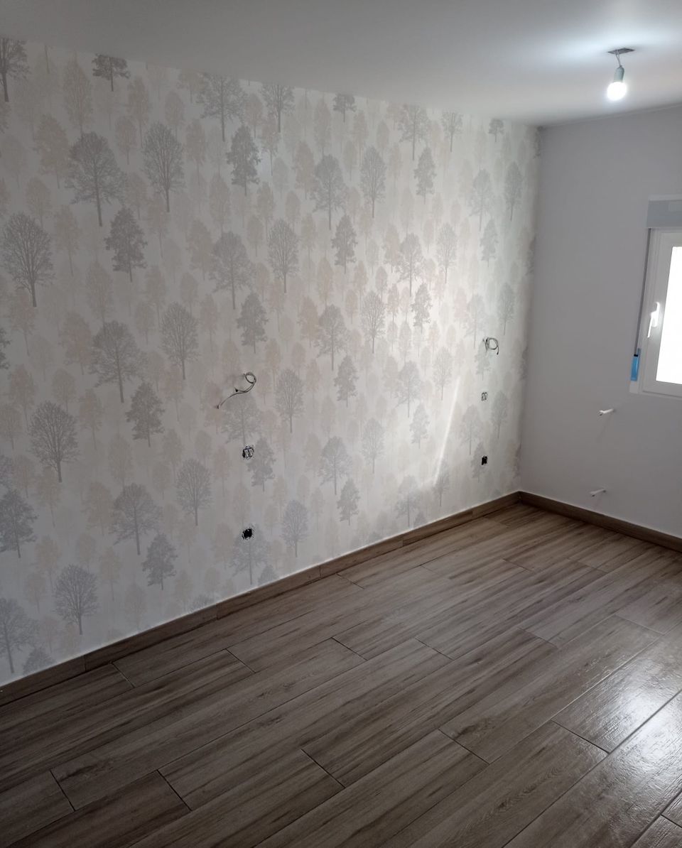 Dormitorio en reforma con papel pintado de árboles en la pared principal y suelo porcelánico efecto madera, a falta de colocar los mecanismos
